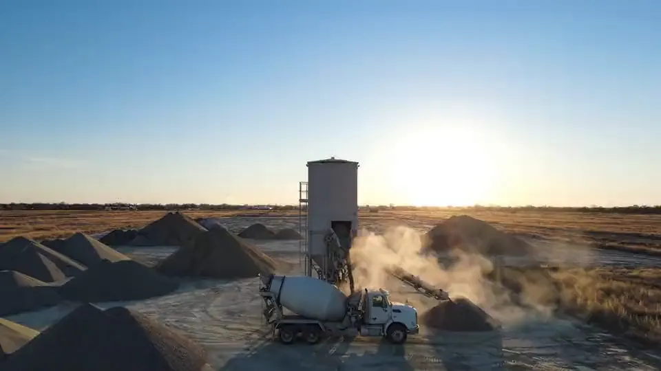Ready-mix truck loading beneath a batch plant silo at sunrise