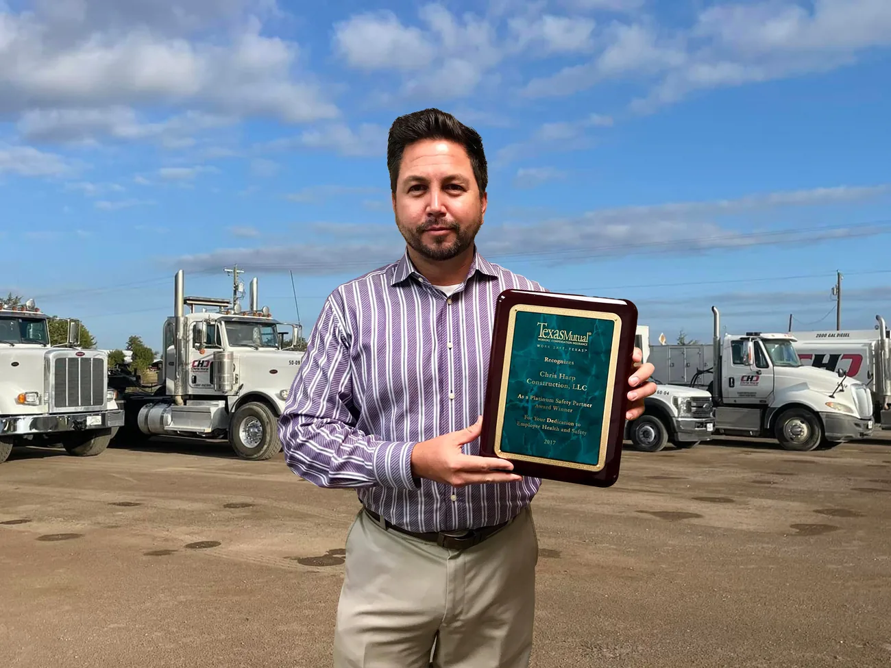 Chris Harp with the Texas Mutual Platinum Safety Partner award plaque in front of the company truck fleet